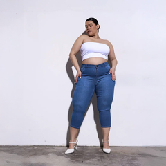 Mujer posando con un top blanco y jeans azules Capri Imelda, en un fondo blanco