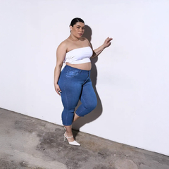 Mujer posando con un top blanco y jeans azul, luciendo zapatos de tacón blancos.