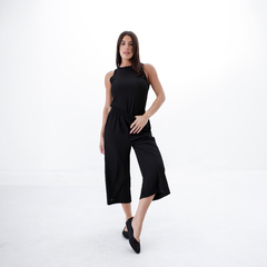 Modelo usando una musculosa negra, combinada con pantalones cortos negros y zapatos negros, posando en un fondo blanco.