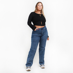 Mujer posando con un conjunto de top negro y jeans rectos azules.