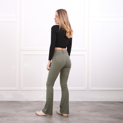 Mujer de espaldas usando un top negro y pantalones de campana verdes, en un fondo blanco.
