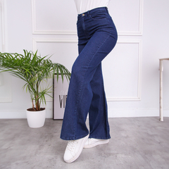 Jeans Anya de tiro alto, color azul oscuro, con corte acampanado, combinados con zapatillas blancas y fondo minimalista.
