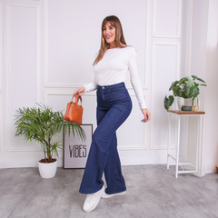 Mujer luciendo jeans Anya de tiro alto, camiseta blanca y zapatillas en un entorno moderno.