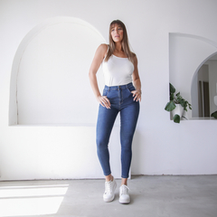Modelo luciendo jeans ajustados de tiro alto, combinados con una camiseta blanca y zapatillas blancas, en un ambiente minimalista.