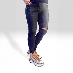 Jeans ajustados de color negro con roturas en las rodillas, combinados con zapatillas de estilo casual.