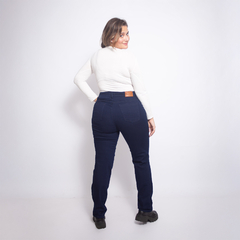 Mujer de espaldas usando jeans azul oscuro y camiseta blanca, de pie en fondo blanco