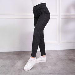 Jeans MOM de color negro, con corte ajustado y cintura alta, combinados con zapatillas blancas en un fondo neutro.