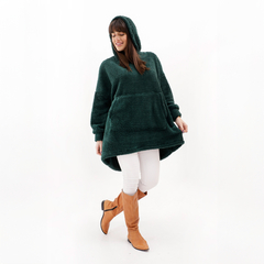 Buzo Maxi Oli de color verde, con capucha y bolsillo frontal, modelo femenino vestido con pantalones blancos y botas altas marrones.