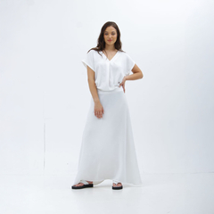 Mujer posando con una maxi falda blanca y blusa blanca en un fondo blanco.
