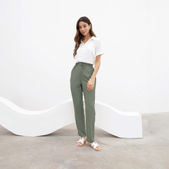 Pantalón Chenoa de color verde, modelo de pie con camiseta blanca y sandalias, en un fondo minimalista
