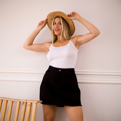 Mujer sonriente con un sombrero de paja, usando una camiseta blanca y una mini falda de jean negra.