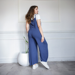 Monos azul con tirantes, visto desde atrás, en un ambiente minimalista con planta decorativa.