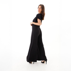 Mono elegante de color negro, con un diseño amplio y moderno, usando tacones altos.