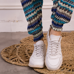 Detalle de un mono con estampado colorido, luciendo con zapatillas blancas sobre una alfombra de fibras naturales.