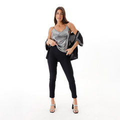 Modelo luciendo una musculosa plateada con tirantes, combinada con pantalones negros y sandalias de tacón, en un fondo blanco.