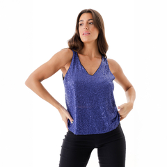 Musculosa Casiopea de color azul con brillo, modelo femenino posando con pantalones oscuros.
