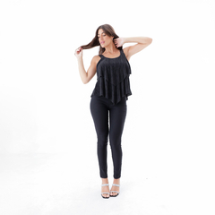 Modelo luciendo una musculosa negra con capas, combinada con pantalones ajustados y sandalias.