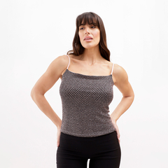 Mujer posando con un top de tirantes finos y un diseño de malla en colores oscuros, combinando con pantalones negros.