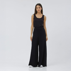 Modelo luciendo una musculosa negra con detalles en los hombros y pantalones anchos en un fondo blanco.