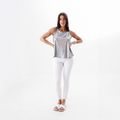 Modelo luciendo una musculosa plateada con tirantes, combinada con pantalones blancos y sandalias, en un fondo blanco.