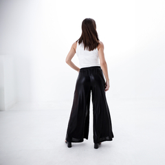 Mujer de espaldas vistiendo palazzos negros con una camiseta blanca, en un fondo blanco.
