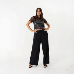 Modelo luciendo una remera negra de estilo cropped con detalles de malla, combinada con pantalones anchos negros y sandalias de tacón.