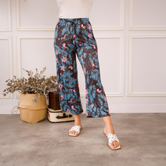 Pantalones Palazzo Daia con estampado floral en tonos azules y rosas, presentados en un ambiente moderno.