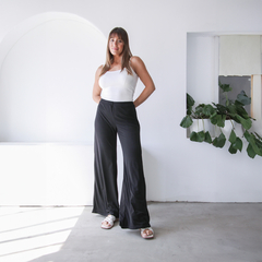 Mujer posando con pantalones palazzo negros y top blanco en un ambiente minimalista.