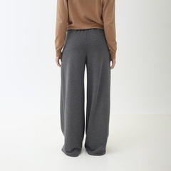 Pantalones palazzo grises vistos desde atrás, combinados con una blusa de manga larga color marrón.