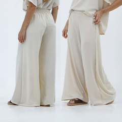 Pantalones palazzo Kalindi en color beige, con cintura elástica y amplio diseño, vistos desde la parte frontal y trasera.