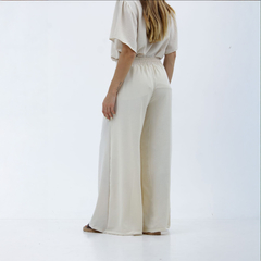 Pantalones palazzo Kalindi en color crema, vistos desde atrás, con una cintura elástica y un diseño amplio.