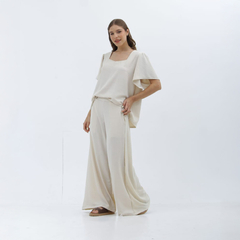 Pantalones palazzo de color beige, con una blusa de manga amplia, modelo posando sobre fondo blanco.