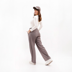 Mujer de pie con pantalones grises y camiseta blanca, mirando hacia atrás, con gorra.