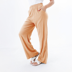 Pantalones palazzo color melaza con cintura elástica y bolsillos, combinados con sandalias blancas.