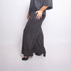 Pantalón palazzo Neus de tela con glitter en color negro, con talle alto y piernas amplias, combinado con un conjunto de top y chaqueta a juego en la misma tela brillante.