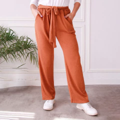 Pantalones Palazzo Vega en color naranja con lazo en la cintura, modelo de mujer con zapatillas blancas.