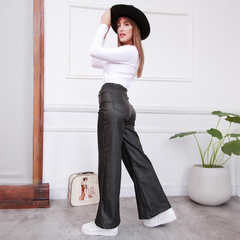 Pantalón Anette en color negro, con una modelo que lleva una camiseta blanca y un sombrero negro, posando en un ambiente moderno.
