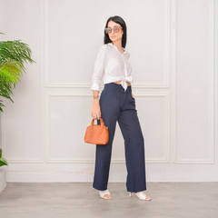 Mujer luciendo pantalón azul marino Azahar, camisa blanca y accesorios, en un entorno elegante.