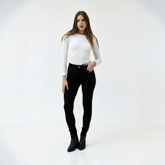 Pantalón Índigo negro ajustado, modelo femenino usando una blusa blanca y botas negras, posando en un fondo blanco.