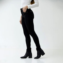 Pantalón índigo negro ajustado con detalles metálicos, combinado con botas negras.