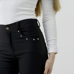 Pantalón Índigo de color negro con detalles de perlas en los bolsillos, usado por una modelo con una blusa blanca.