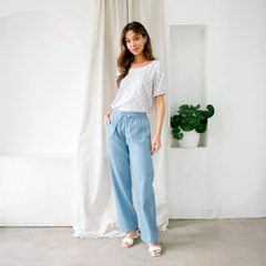 Mujer usando pantalón Lorena de color celeste, con una blusa blanca, en un ambiente luminoso y moderno.