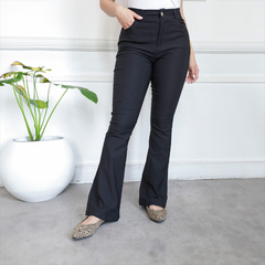 Pantalón Nasha negro, ajustado y de bota ancha, en un entorno moderno con planta decorativa.