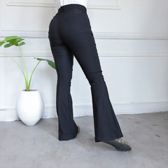 Pantalón Nasha negro de corte acampanado visto desde atrás, con detalles de bolsillos y una planta decorativa al lado.