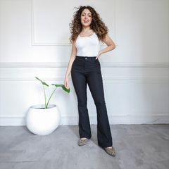 Mujer sonriente usando pantalón negro Nasha, con una camiseta blanca, en un ambiente iluminado.