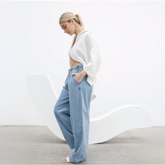 Mujer luciendo un pantalón pijama jean de corte amplio, con una camisa blanca, en un entorno minimalista.