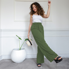 Modelo luciendo un pantalón sastrero verde Lupe, con una blusa blanca, sosteniendo un sombrero y posando en un ambiente elegante.
