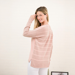 Una modelo sonriente usando un suéter rosa claro con rayas, de espaldas, en un fondo blanco.