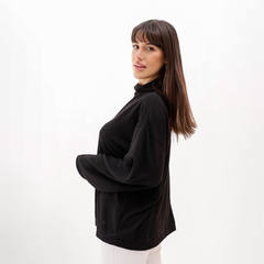 Modelo luciendo una polera lanilla negra con cuello alto y mangas amplias, de perfil.
