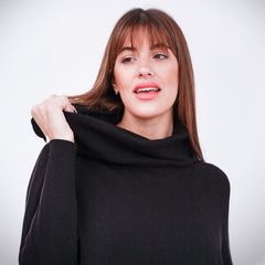 Modelo usando un polerón negro con cuello alto, sonriendo y tocándose el cabello.